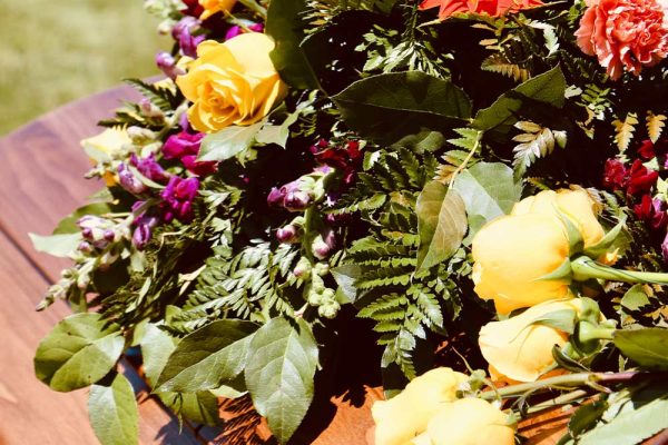 Close up of flower bouquet on coffin with people wearing black in background, outdoor funeral ceremony, copy space