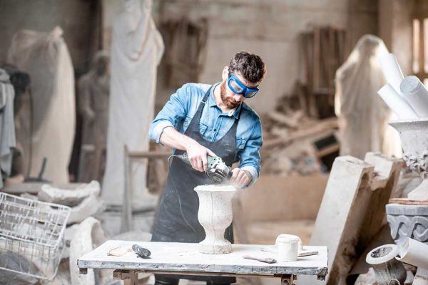 Sculptor in workware grinding stone vase at the working space in the old atmospheric studio